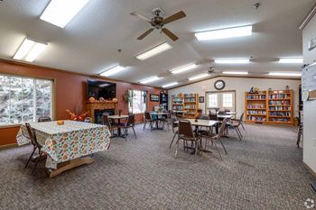 A room with a carpeted floor, a ceiling fan, and a bookshelf filled with books.